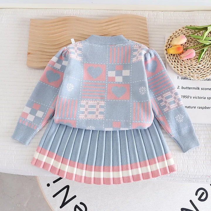 Blue two-piece knit outfit laid flat, showing patterned sleeves and a pleated skirt with pink-and-white hem stripes