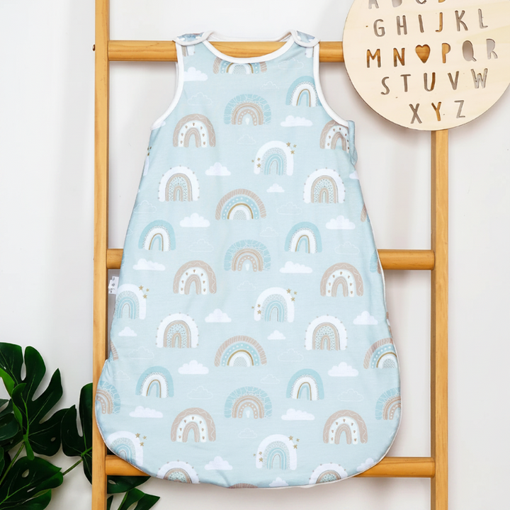Light blue rainbow-print sleeveless baby sleep sack hanging from a wooden ladder