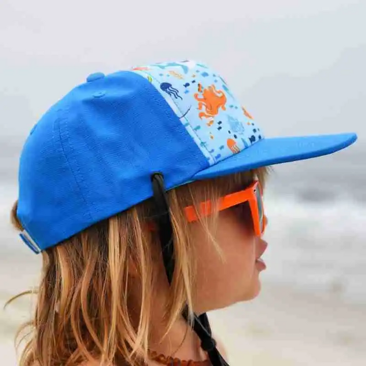 Side view of a child wearing a blue sea-animal cap with a flat brim and chin strap