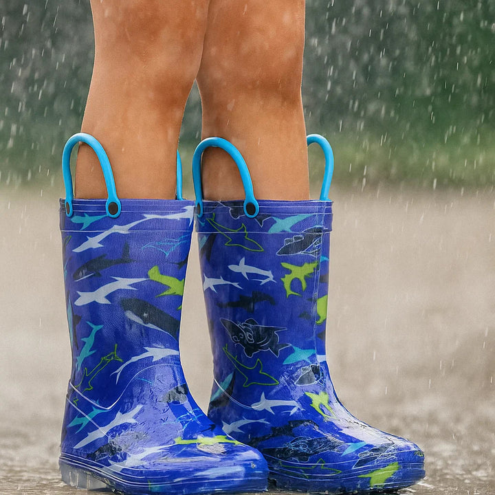 Child standing in the rain wearing blue shark-print boots with blue loops