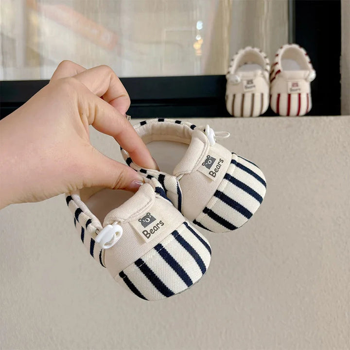 Blue-and-cream striped baby shoes held by their openings