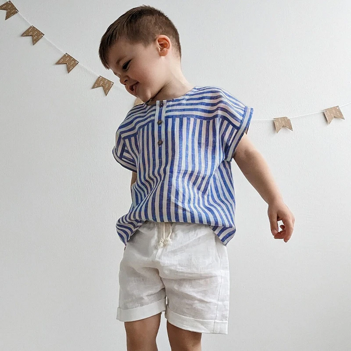 Boy standing in a blue striped button-detail shirt with white shorts