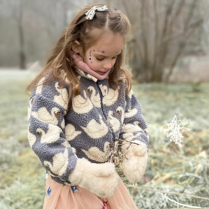 Child wearing a blue swan-print fleece jacket outdoors with mittens