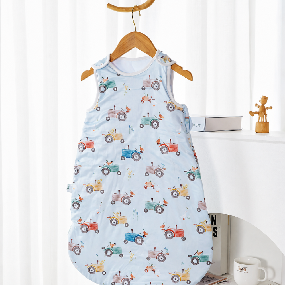 Light blue baby sleep sack with colorful tractor prints on a wooden hanger