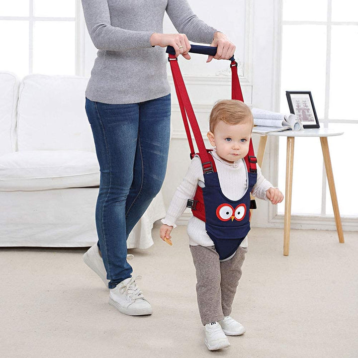 Child practicing walking in a blue harness while an adult holds the padded handle