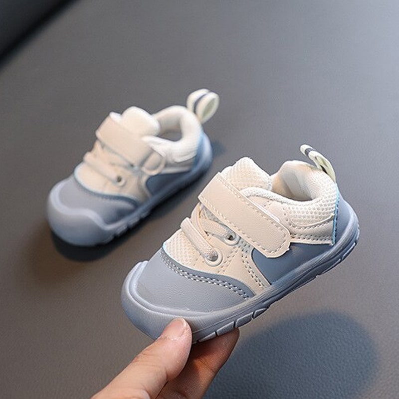 Blue and white baby sneakers, with one shoe held to show the rounded toe and strap