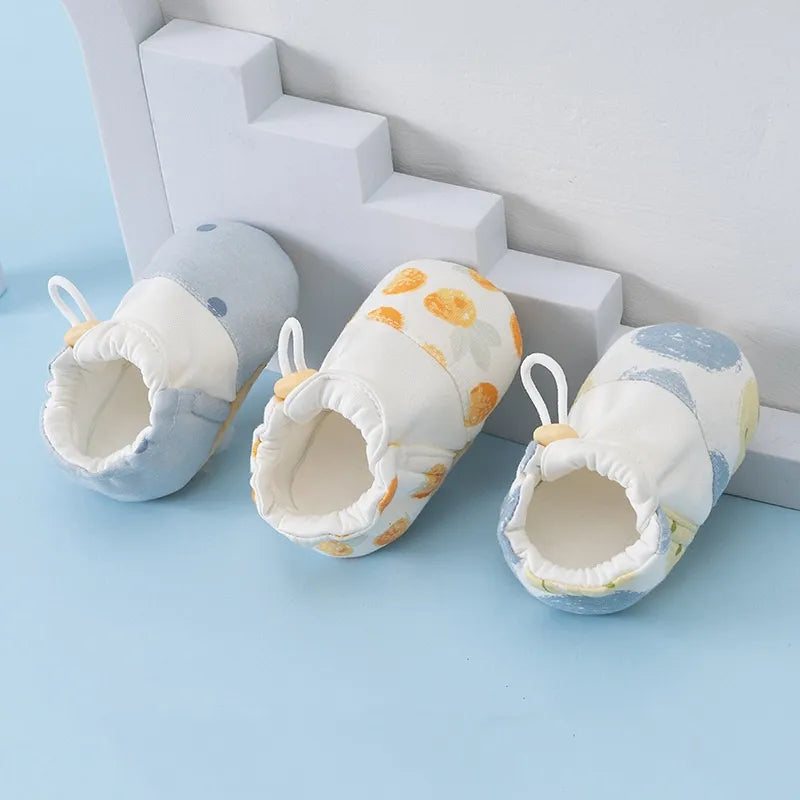 Three baby shoes in blue and yellow prints beside white display steps