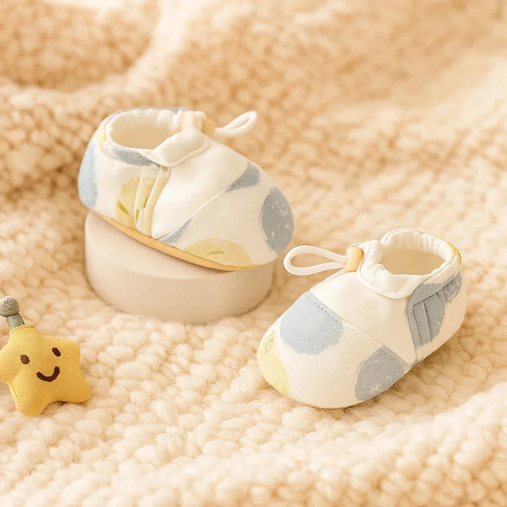 Blue-and-yellow dot-print baby shoes displayed on a cream knit blanket