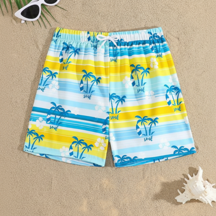 Blue, yellow, and white striped swim trunks with palm tree prints laid on sand