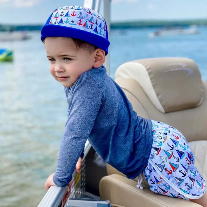 Child wearing a blue boats-and-anchors cap while sitting on a boat