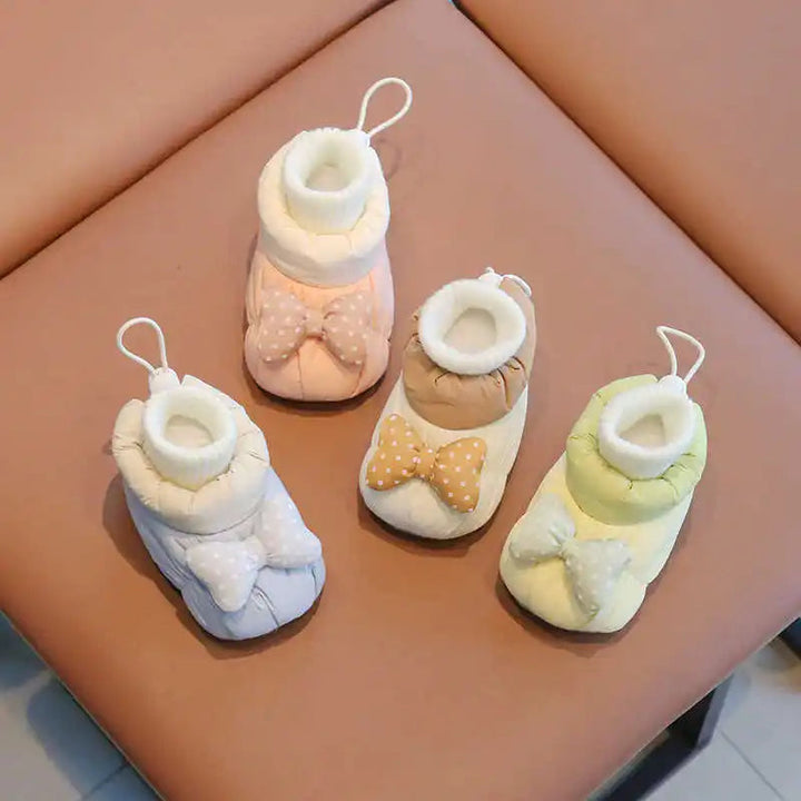 Pink, white, green, and pale blue baby shoes with ribbed cuffs and front bows on a chair