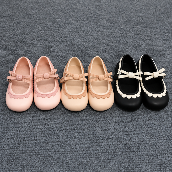 Pink, apricot, and black bow Mary Jane shoes with scalloped trim arranged on gray carpet