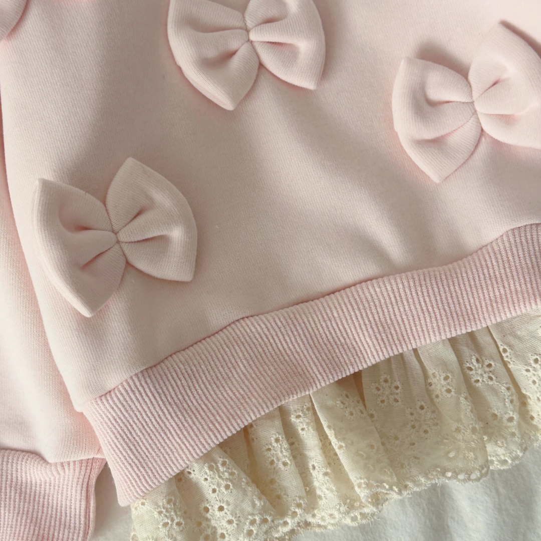 Close-up of pink sweater bows, ribbed hem band, and cream lace edging
