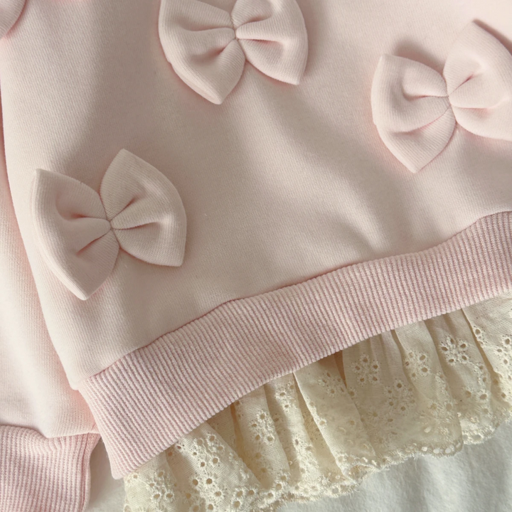 Close-up of pink sweater bows, ribbed hem band, and cream lace edging