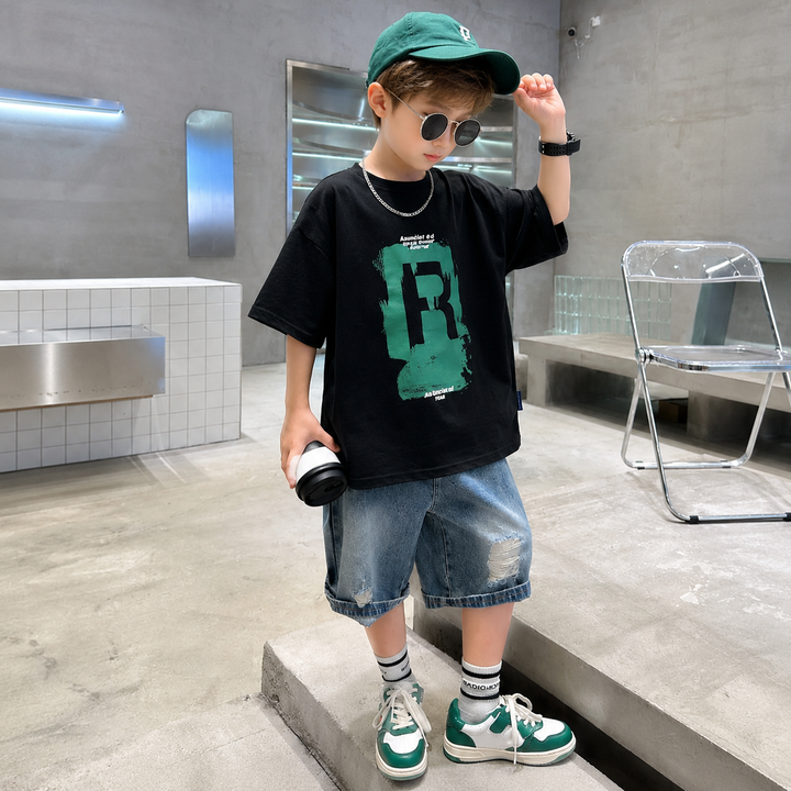 Boy wearing a black T-shirt with a green R graphic and blue denim shorts.