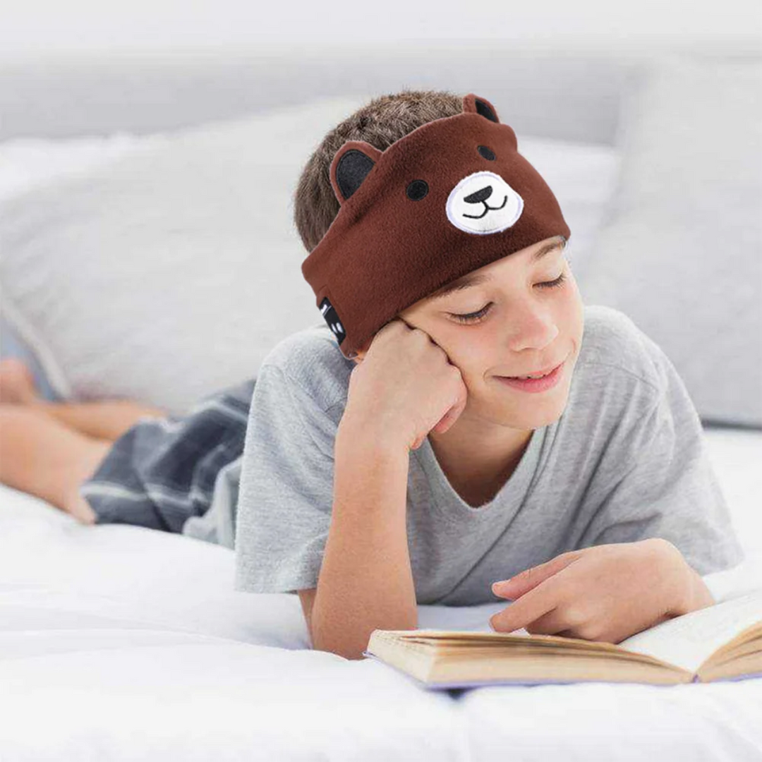 Child reading in bed with a brown bear Bluetooth mask worn above the eyes.