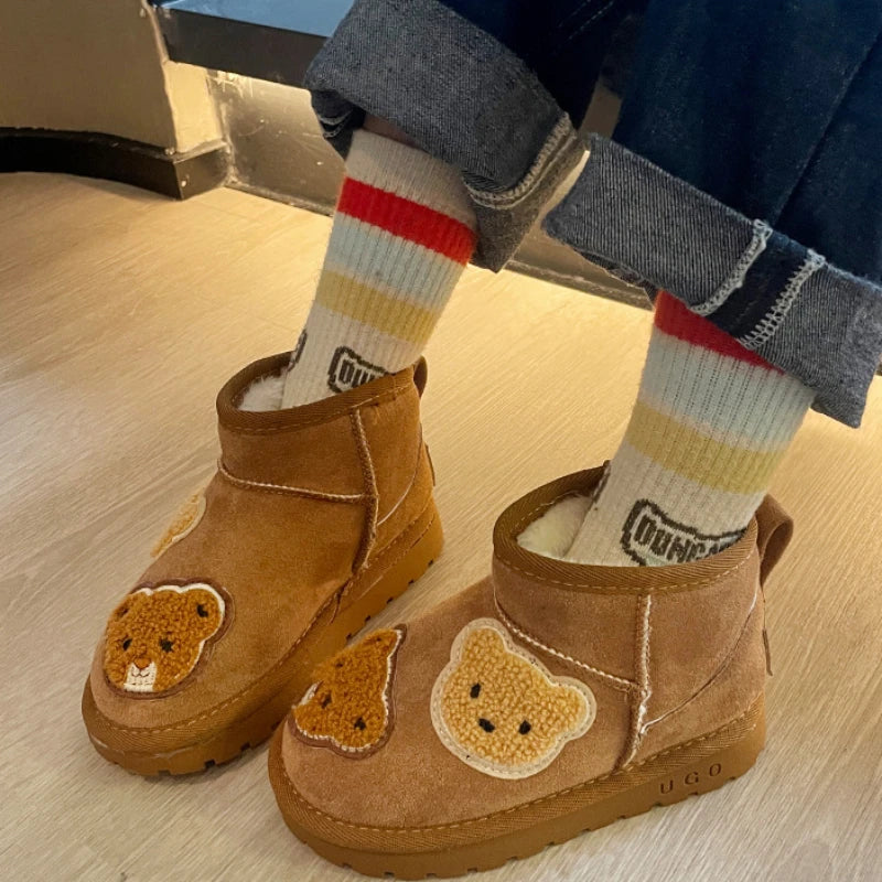 Bear-patch ankle boots worn with striped socks on a wood floor