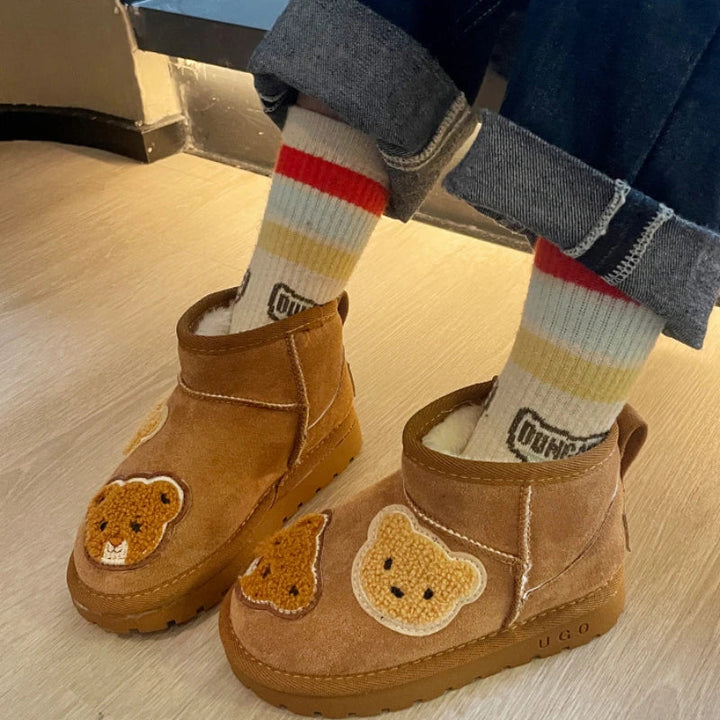 Bear-patch ankle boots worn with striped socks on a wood floor