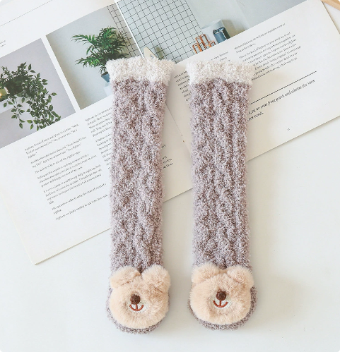Brown long baby socks with bear faces and cream cuffs arranged on an open book.