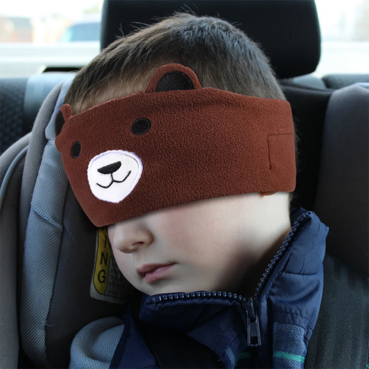 Child resting in a car seat with the brown bear sleep mask covering the eyes.