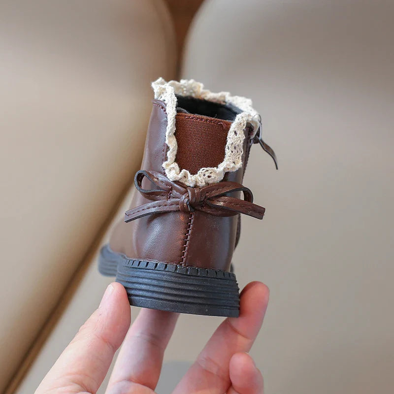 Back of a brown ankle boot with a decorative bow and cream ankle trim