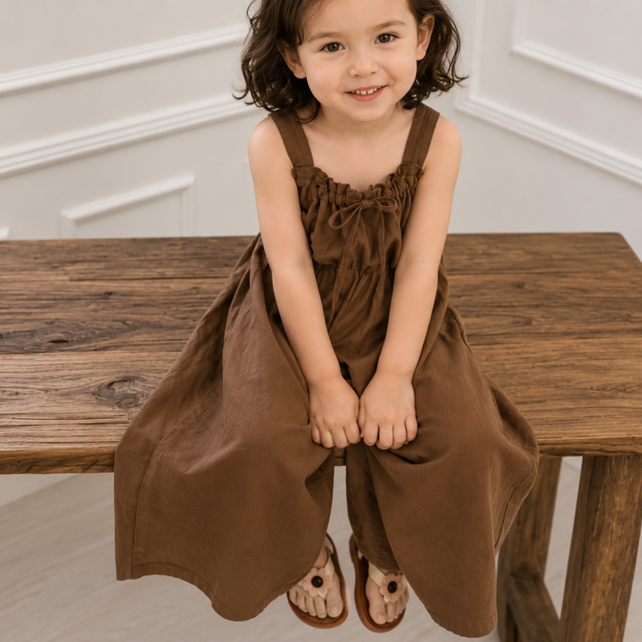 Child seated on a wooden bench wearing the brown bow jumpsuit
