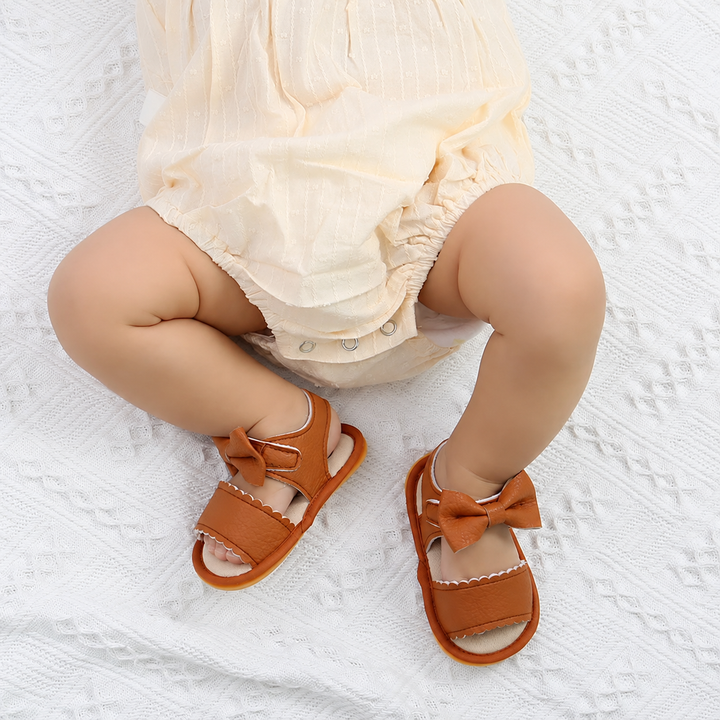 Baby in a light summer outfit wearing brown bow sandals