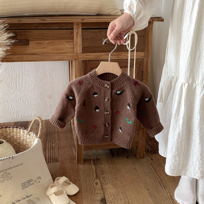 Brown knit cardigan with small colorful motifs hanging from a wooden hanger