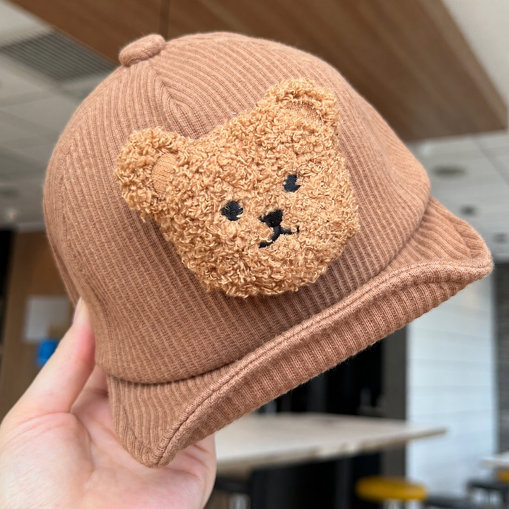 Brown corduroy baby cap held to show the fuzzy bear face and curved brim