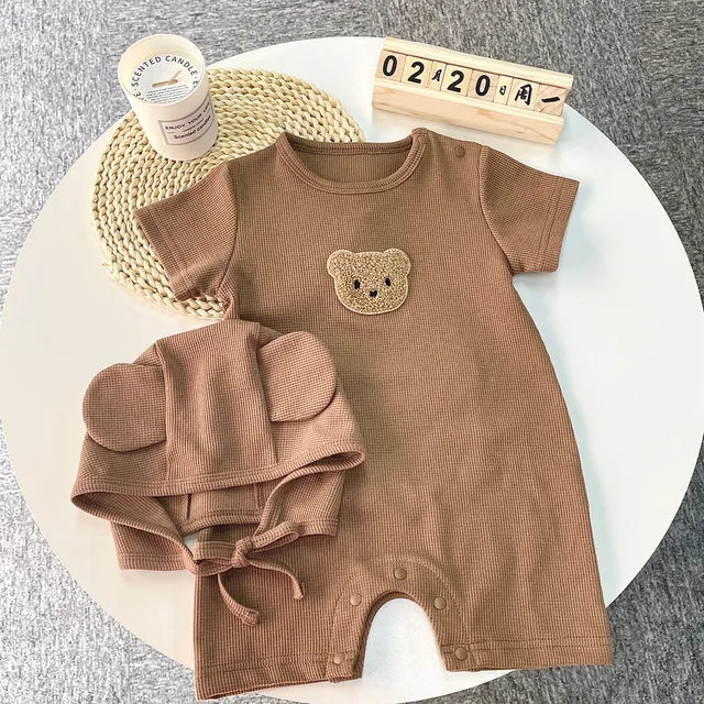 Brown cotton baby romper and matching hat arranged on a round table