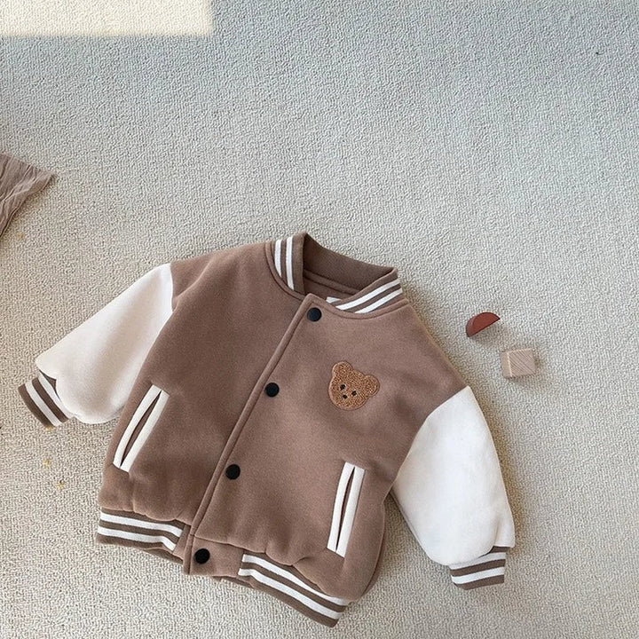 Front of a brown and cream baseball jacket with striped pockets and a bear patch