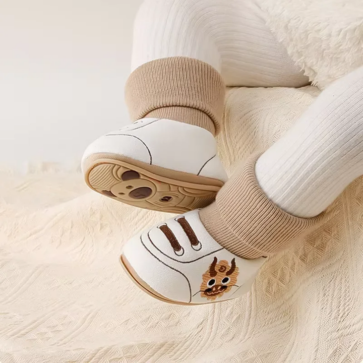 Baby wearing brown-cuff shoes, with one patterned sole turned outward.