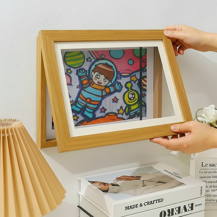 Hands holding open a brown art frame with an astronaut drawing