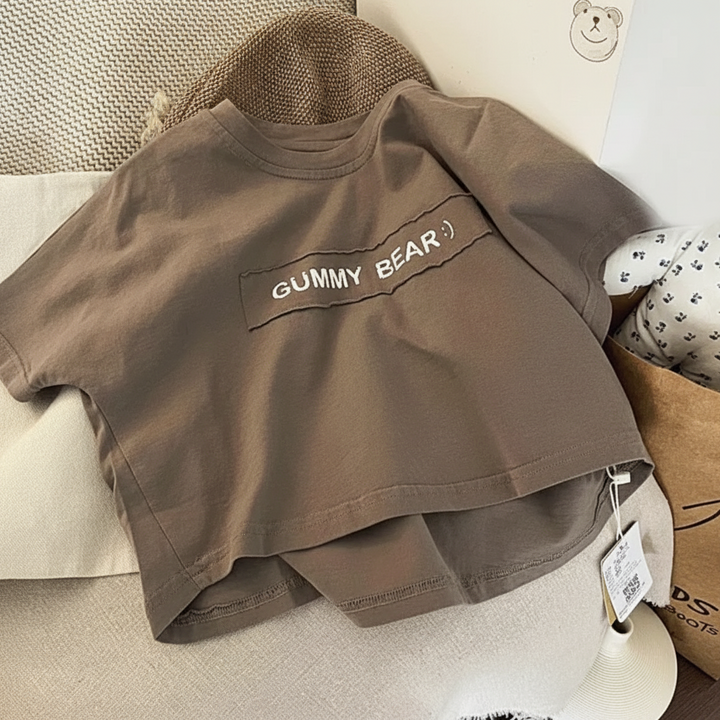 Brown short-sleeve T-shirt on a chair, showing the front lettering and curved back hem