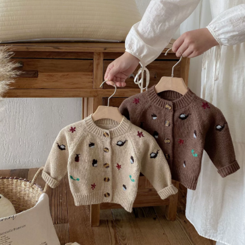 Brown and khaki knit cardigans with colorful motifs and button fronts displayed on hangers