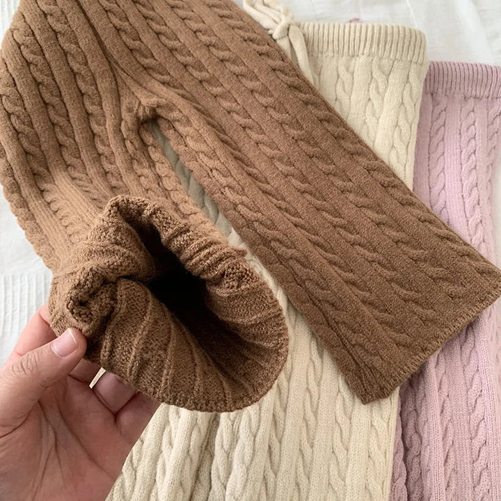 Close-up of a brown cable-knit pant leg held open over beige and pink pants