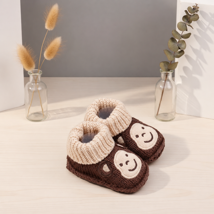 Brown monkey knitted booties with beige cuffs, shown at an angle