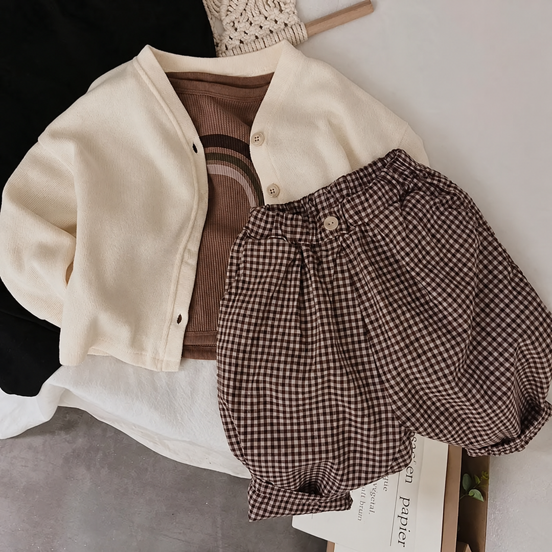 Brown rainbow T-shirt layered under a beige cardigan beside gingham shorts