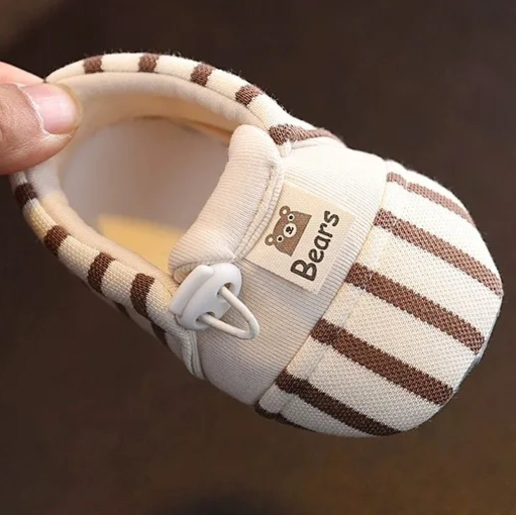 Close-up of a brown striped baby shoe with an elastic closure and bear detail