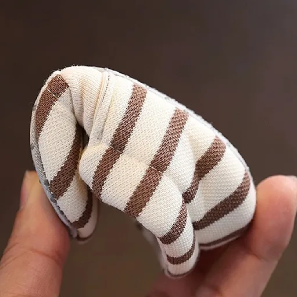 Brown striped baby shoe bent to show its flexible fabric construction