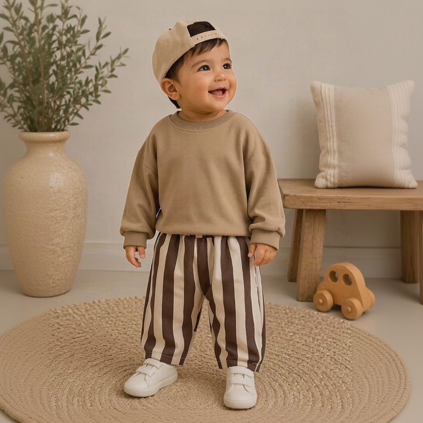 Toddler wearing brown and cream striped pants with a beige sweatshirt indoors