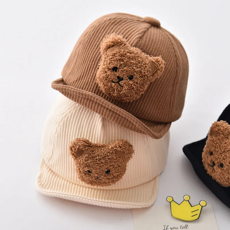 Brown and white bear-face corduroy caps stacked beside a partially visible black cap