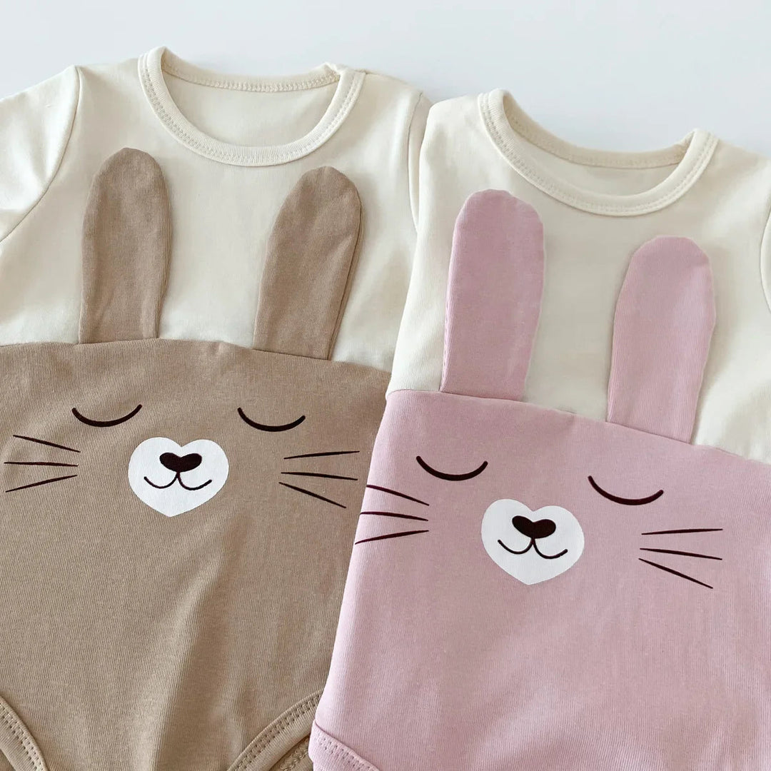 Close-up of bunny faces and fabric ears on brown and pink baby bodysuits