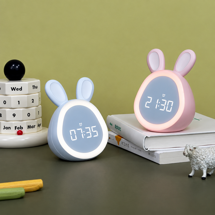 White and pink bunny digital alarm clocks beside books on a desk