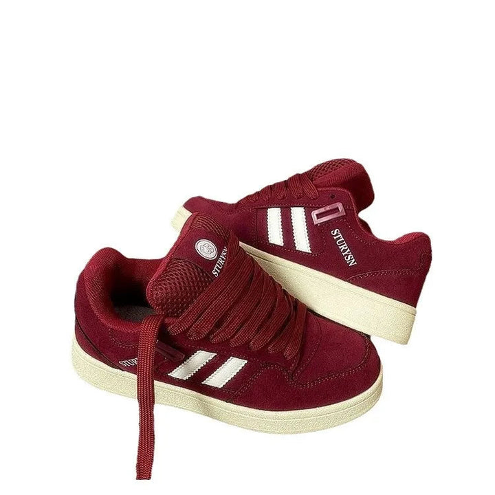 Pair of burgundy low-top sneakers with white side stripes on a white background