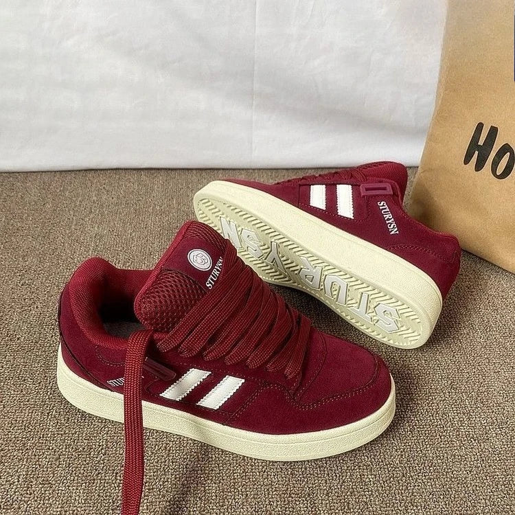 Burgundy sneakers on carpet with one shoe tilted to show the cream-colored outsole
