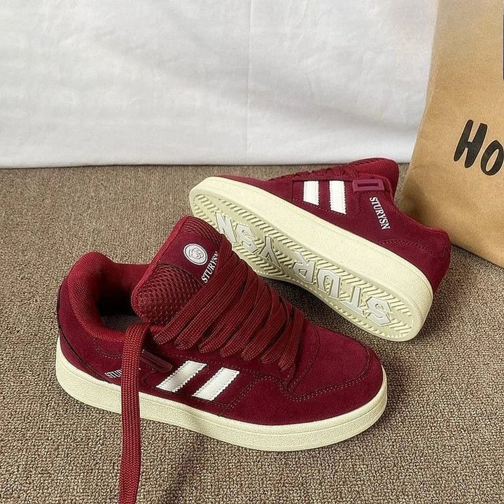 Burgundy sneakers on carpet with one shoe tilted to show the cream-colored outsole