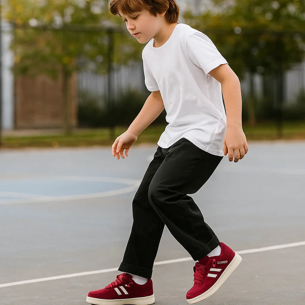 Child wearing burgundy low-top sneakers with a white T-shirt and black pants on an outdoor court