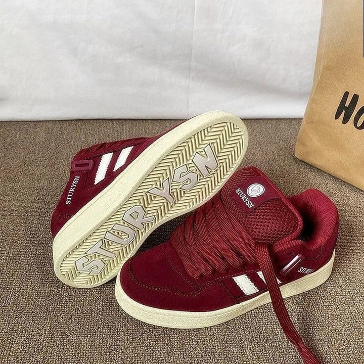 Pair of burgundy sneakers showing ribbon-style laces and the patterned rubber outsole