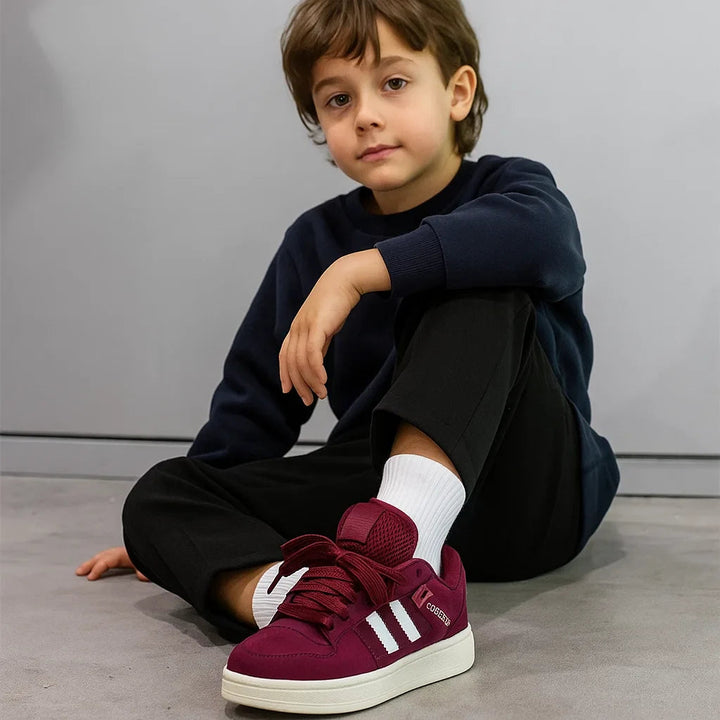 Seated child wearing burgundy sneakers with white side stripes and cream-colored soles